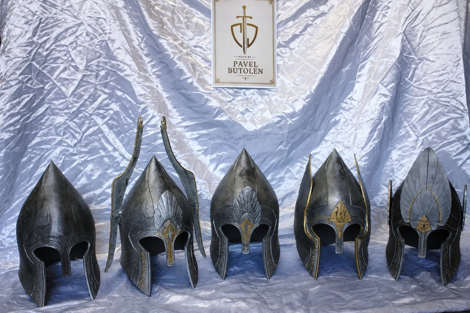 Five dark helmets with tall crests on silver fabric