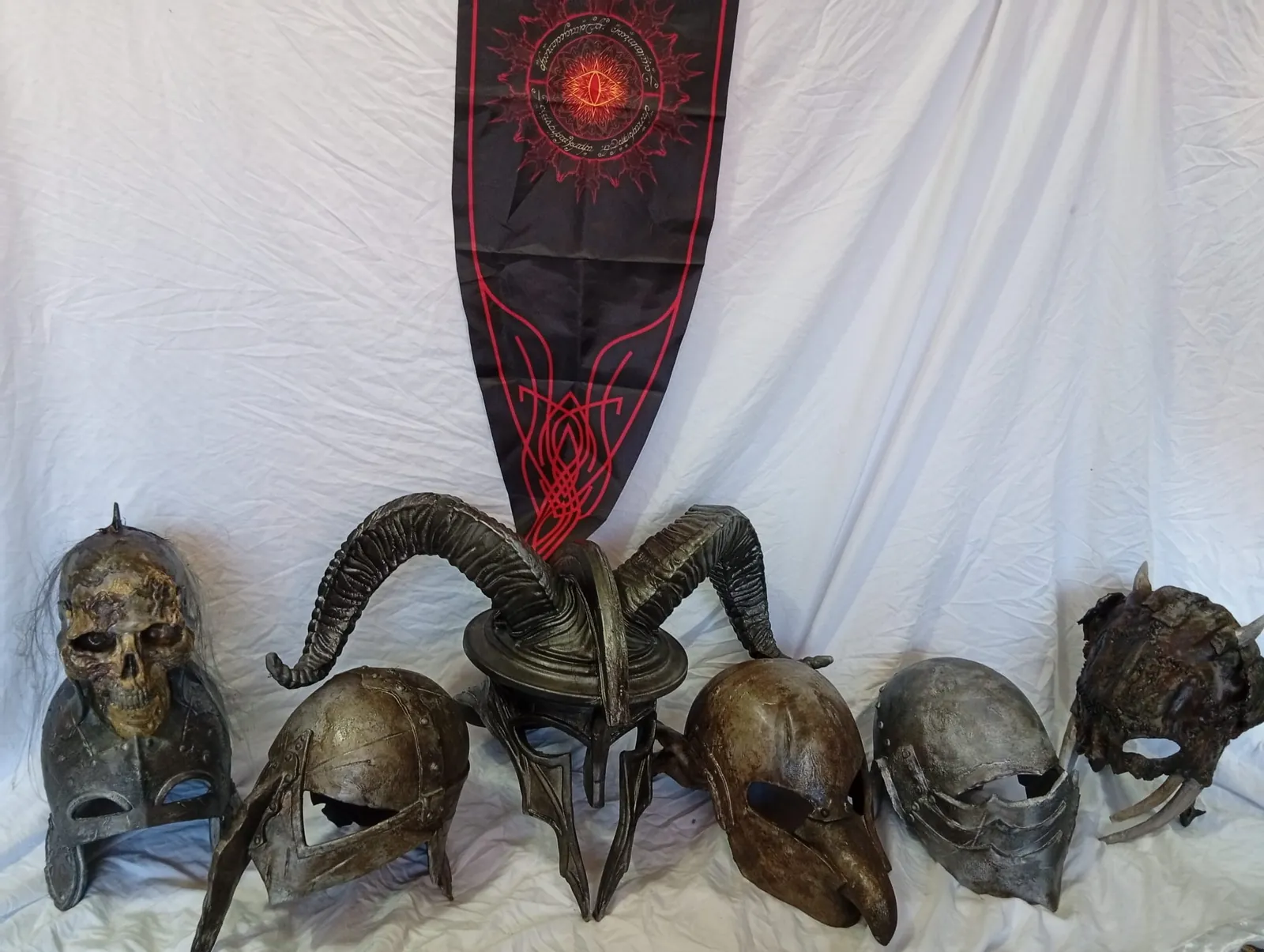 Six dark fantasy helmets in front of a banner with the Eye