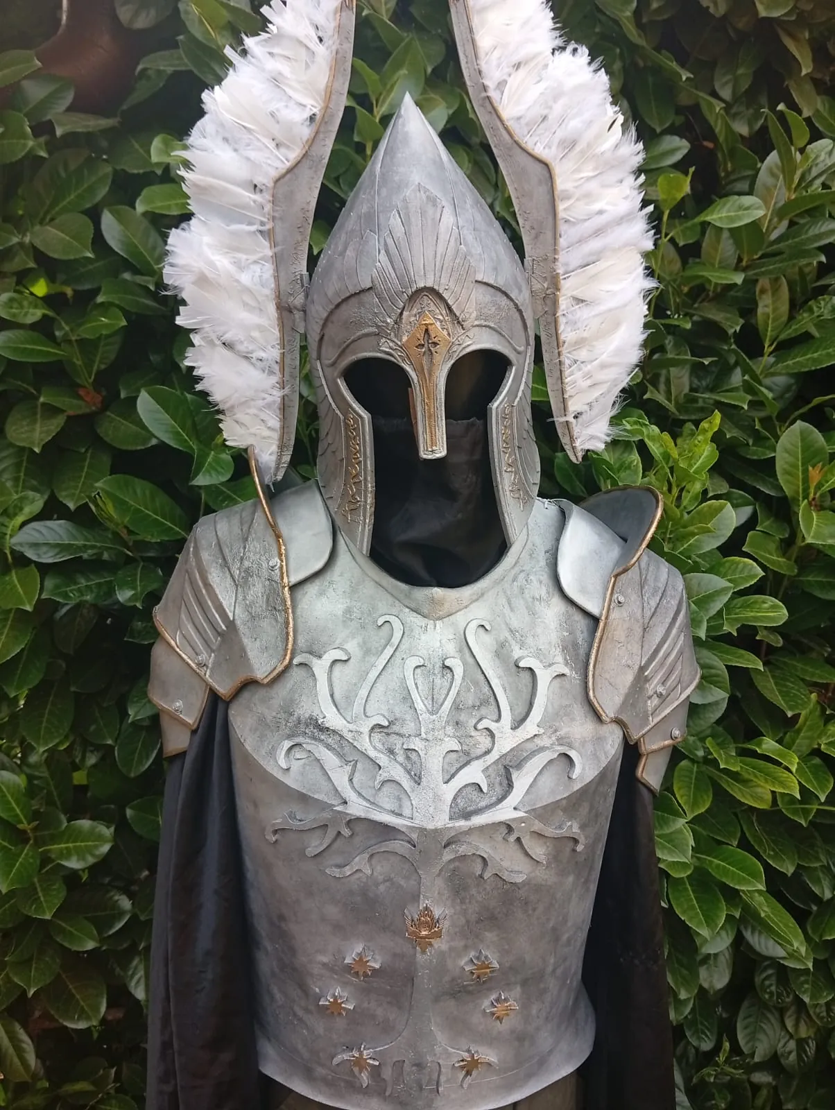 Armor with the White Tree and a winged helmet in front of greenery